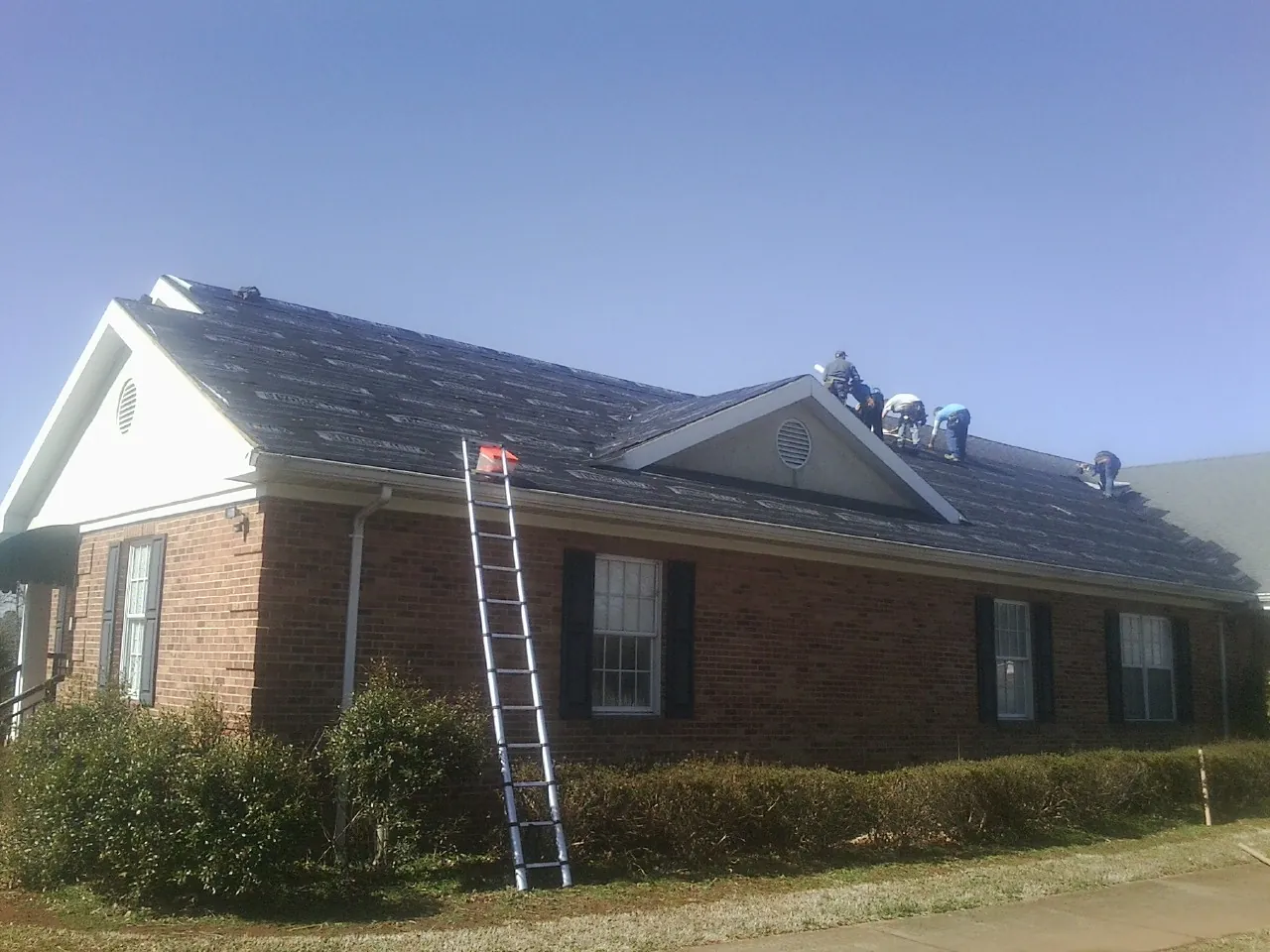 Crew tearing shingles off a brick ranch roof with a ladder set — Emergency Roof Repair work by our crew in Elkhart