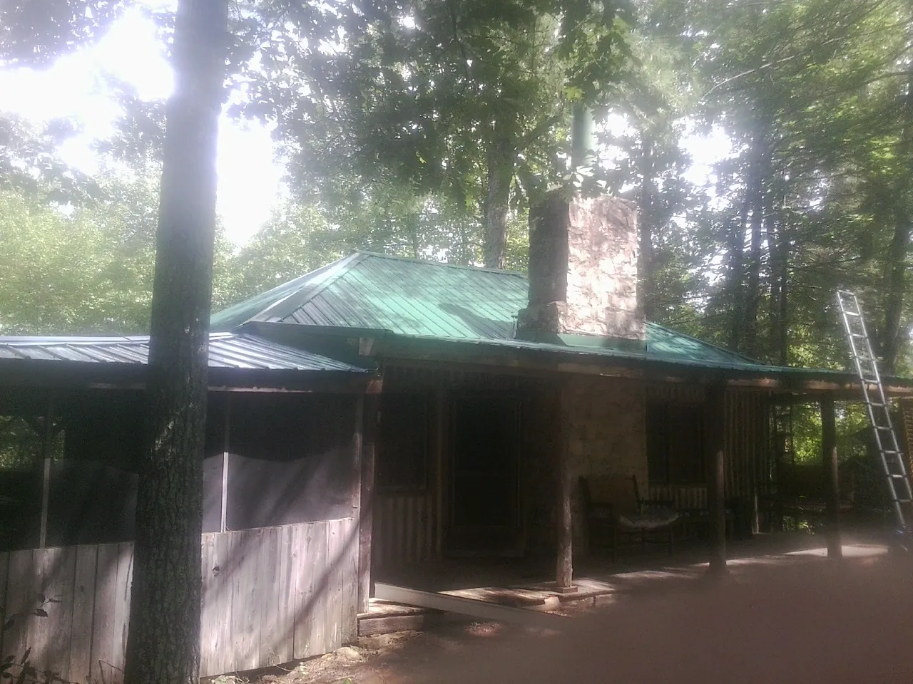 Green metal roof and stone chimney above a log cabin porch in Elkhart