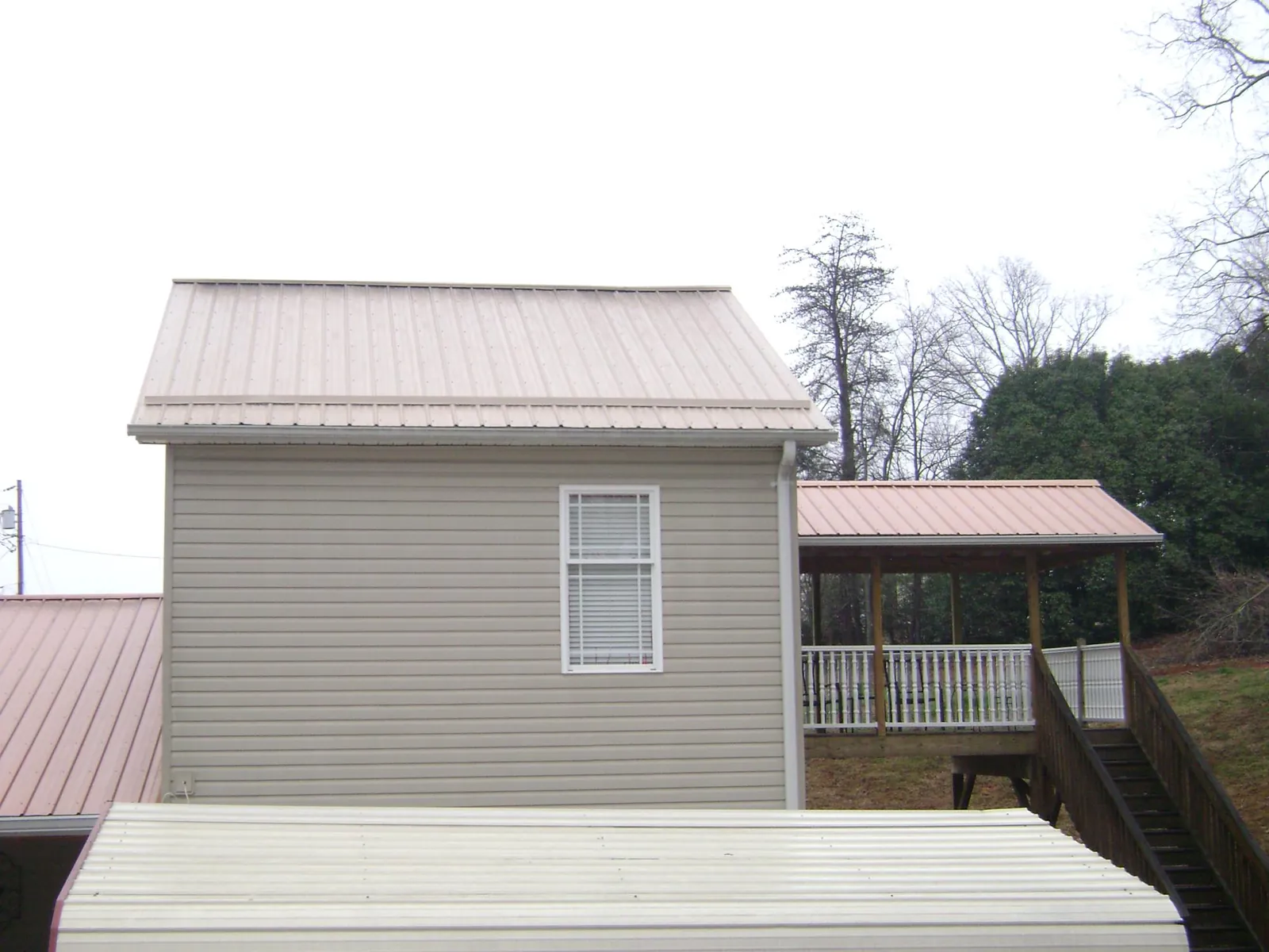 Tan metal roofs on a two story addition and attached porch, from a Roof Replacement job in Elkhart